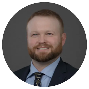 Professional headshot of a smiling bearded man in suit