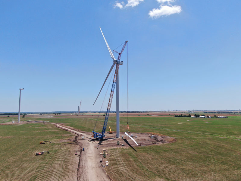 Crane installing wind turbine blades in farmland